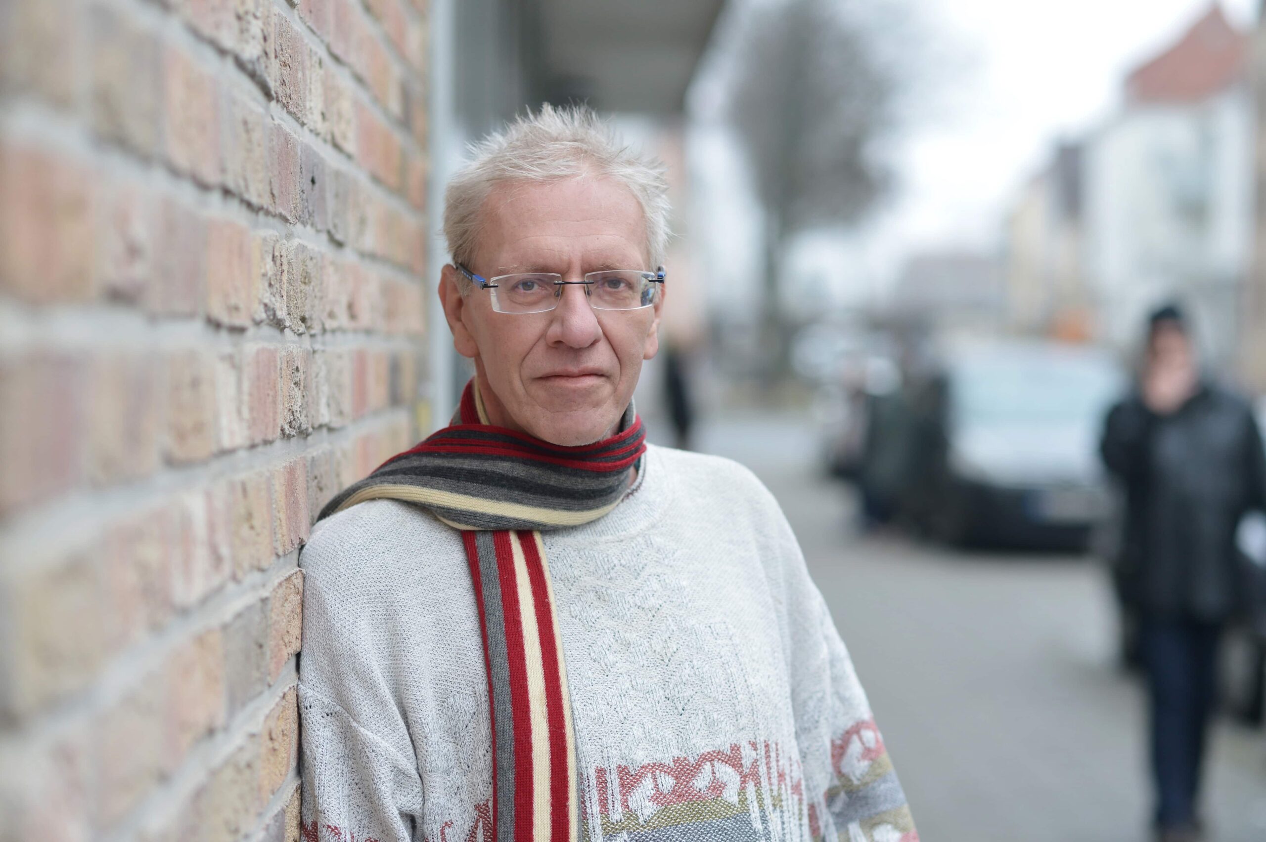 Betreuungshelfer Markus Urban mit gestreiftem Schal und Brille, neben einer Backsteinwand