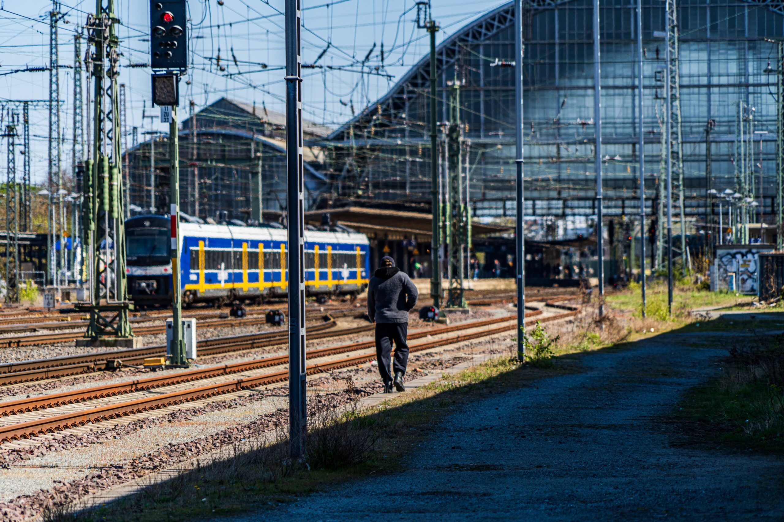 Bremer Bahnhof im äußeren Gleisbereich. Ein Mensch in grauen Klamotten geht an den Gleisen Richtung Bahnhof entlang.